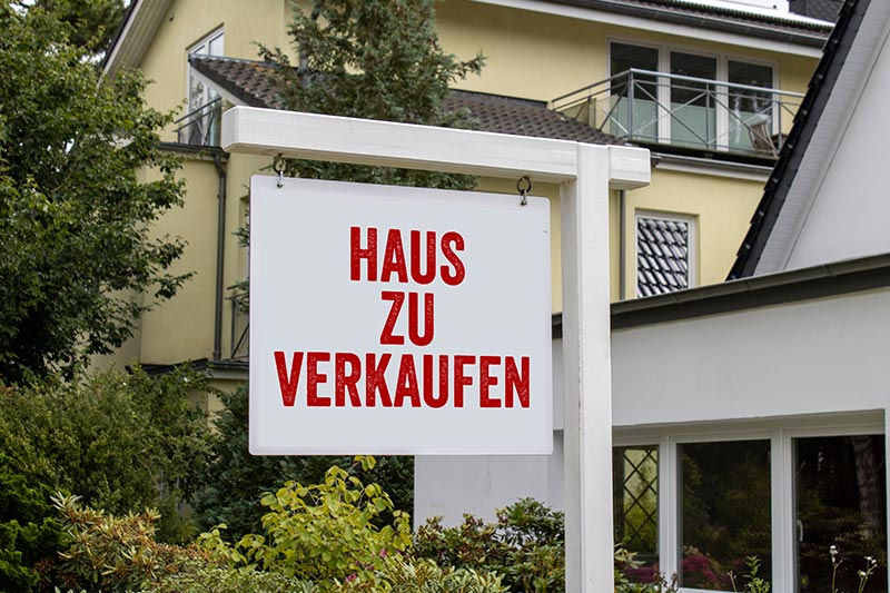 Schild vor einem Haus auf dem steht Haus zu verkaufen