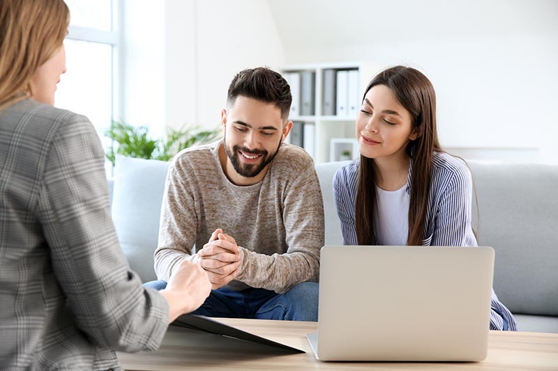 Immobilienmaklerin Riedberg sitzt mit einem Paar an einem Tisch und zeigt etwas auf einem Laptop